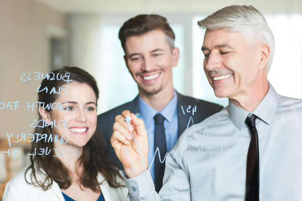 Imprenditore senior e due collaboratori più giovani lavorano insieme su una lavagna trasparente